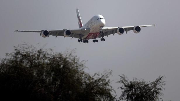 Ein großes Passagierflugzeug mit ausgefahrenem Fahrwerk fliegt niedrig über Bäumen im Anflug.