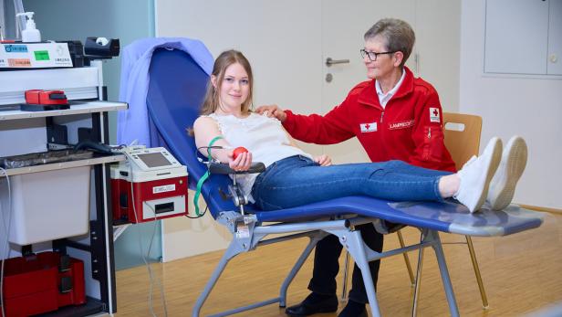 Eine junge Frau spendet Blut auf einer Liege, während eine Mitarbeiterin des Roten Kreuzes sie betreut.