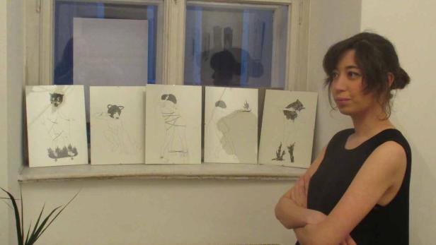 Eine junge Frau steht vor einer Fensterbank mit fünf Zeichnungen.