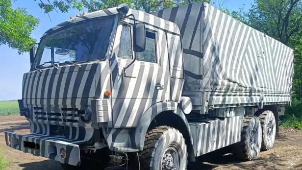 Russischer Lastwagen mit auffälligem Zebramuster steht auf einem Feldweg neben Bäumen.