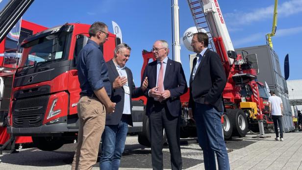Vier Männer im Gespräch vor modernen Feuerwehrfahrzeugen mit ausfahrbaren Drehleitern auf der Interschutz-Messe in Hannover.