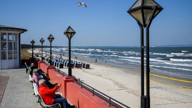 Mehrere Personen sitzen auf Bänken und blicken auf das Meer.