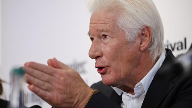 Richard Gere mit grauem Haar gestikuliert und schaut zur Seite.