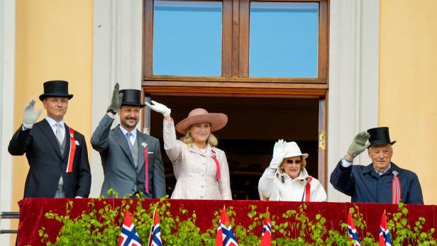 Die norwegische Königsfamilie winkt elegant gekleidet von einem Balkon.