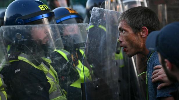 Ein verletzter Mann mit blutigem Gesicht steht einer Reihe von BTP-Polizisten mit Schutzschilden gegenüber.