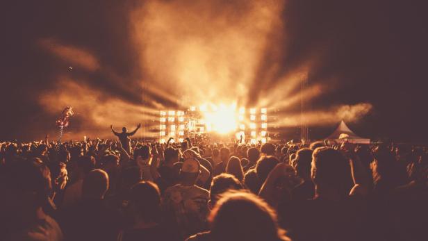 Menschenmenge bei einem nächtlichen Open-Air-Konzert mit heller Bühnenbeleuchtung.
