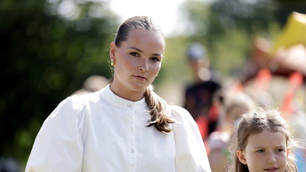 Prinzessin Ingrid Alexandra mit weißer Bluse und ein Mädchen stehen im Freien, im Hintergrund sind weitere Menschen unscharf zu sehen.