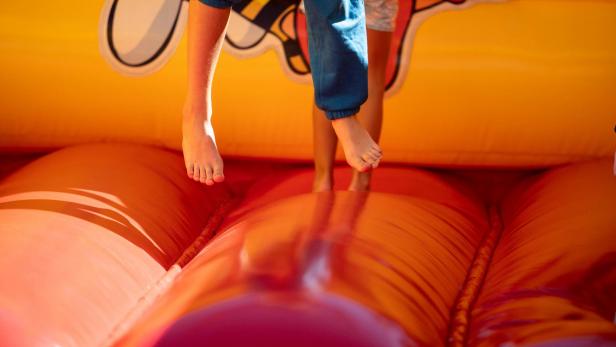 Kinder springen barfuß auf einer bunten Hüpfburg.