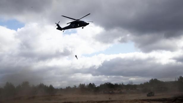 Hubschrauber schwebt über einem sandigen Gelände, während sich eine Person an einem Seil aus der Luft abseilt.