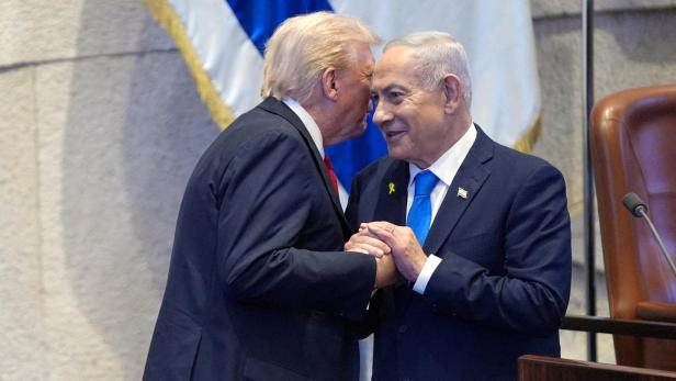 Donald Trump flüstert Benjamin Netanjahu etwas ins Ohr, während sie sich die Hände halten.