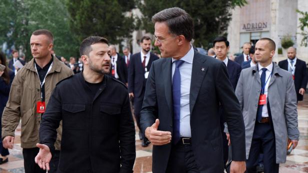 Wolodymyr Selenskyj und Mark Rutte gehen im Gespräch über einen Platz, umgeben von Sicherheitskräften.