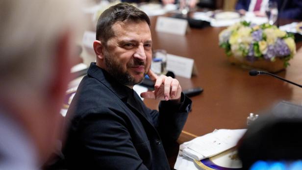Wolodymyr Selenskyj sitzt in dunkler Kleidung an einem Konferenztisch und blickt aufmerksam zur Seite.