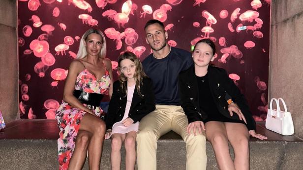 Marko Arnautovic sitzt mit Partnerin Sarah und den beiden Töchtern Alicia und Emilia vor einem Aquarium mit Quallen.