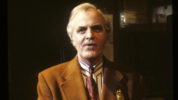 James Handy mit grauen Haaren trägt einen braunen Mantel