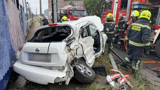 Das Wrack eines weißen Auto neben Feuerwehrmännern
