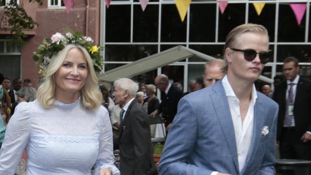 Kronprinzessin Mette-Marit von Norwegen mit Blumenkranz und Marius Borg Høiby in einem hellblauen Sakko bei einer Veranstaltung im Freien.
