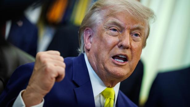 Donald Trump spricht mit erhobener Faust und ernstem Gesichtsausdruck in einem Raum.