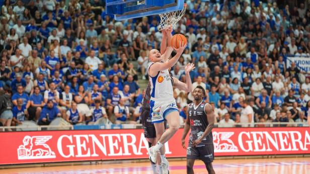 Ein Basketballspieler im weißen Trikot springt zum Korbleger, während ein Verteidiger im schwarzen Trikot versucht zu blocken.