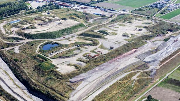 Luftaufnahme einer weitläufigen Deponie mit unebenem Gelände, kleinen Wasserflächen und angrenzenden landwirtschaftlichen Feldern.