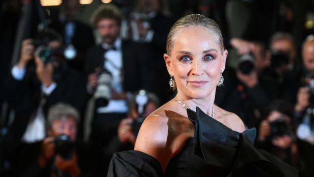 Sharon Stone posiert in einem eleganten schwarzen Kleid vor einer Gruppe von Fotografen.