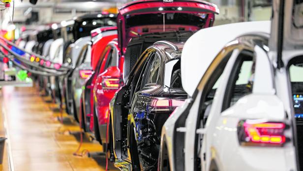 Mehrere Autos stehen hintereinander in einer Fabrikhalle, mit geöffneten Türen und Kofferräumen auf einer Produktionslinie.