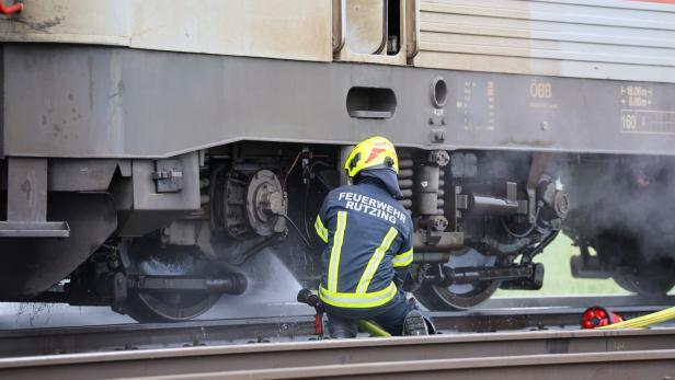 Ein Feuerwehrmann löscht mit einem Schlauch einen Brand am Fahrwerk eines Zuges auf den Gleisen.