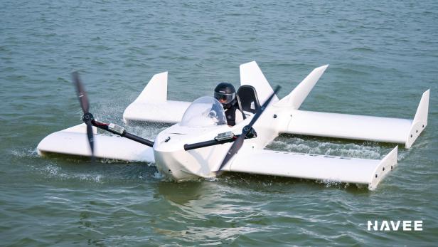 Kleines weißes Bodeneffektfahrzeug mit Propellern fährt auf dem Wasser, eine Person sitzt darin.