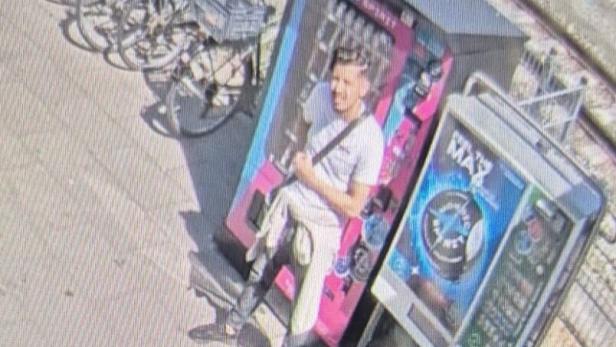Ein Mann steht bei einem Automaten neben abgestellten Fahrrädern an einem sonnigen Bahnsteig.