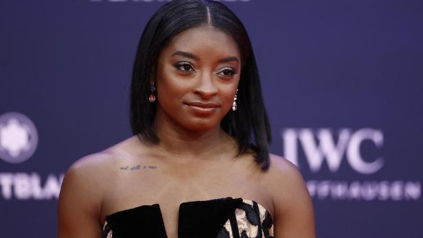 Simone Biles posiert vor einem dunkelblauen Hintergrund mit dem Schriftzug #Laureus25 und dem Logo von IWC Schaffhausen.