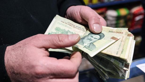 Hände halten einen Stapel iranischer 100.000-Rial-Banknoten mit dem Porträt von Ayatollah Khomeini.