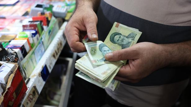 Eine Person hält einen Stapel iranischer Rial-Banknoten mit dem Porträt von Ayatollah Khomeini in den Händen.