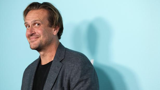 Jason Segel lächelt vor einem hellblauen Hintergrund in die Kamera.