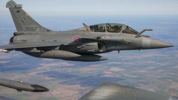 Kampfjet mit zwei Piloten im Cockpit fliegt über eine ländliche Landschaft.