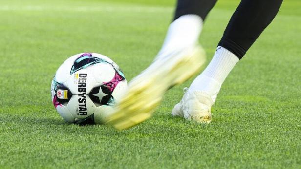Ein Fußballspieler mit weißen Schuhen schießt einen Ball auf grünem Rasen.