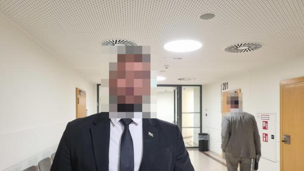 Zeuge Achmad in Anzug in einem Gang des Wiener Landesgericht, sein Gesicht ist verpixelt.