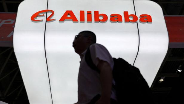 Die Silhouette einer Person geht vor einem beleuchteten, weißen Schild mit dem roten Alibaba-Logo entlang.