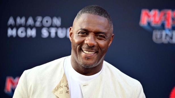 Idris Elba lächelt vor einem Hintergrund von Amazon MGM Studios in die Kamera.