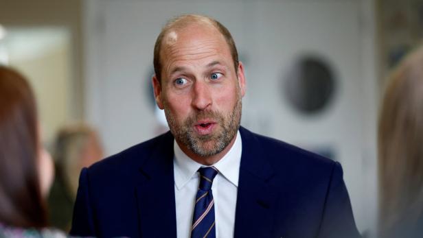 Prinz William trägt einen dunkelblauen Anzug mit Krawatte und spricht in einem Gespräch mit anderen Personen.