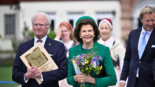 König Carl XVI. Gustaf und Königin Silvia von Schweden bei einem öffentlichen Auftritt, wobei die Königin einen Blumenstrauß hält.