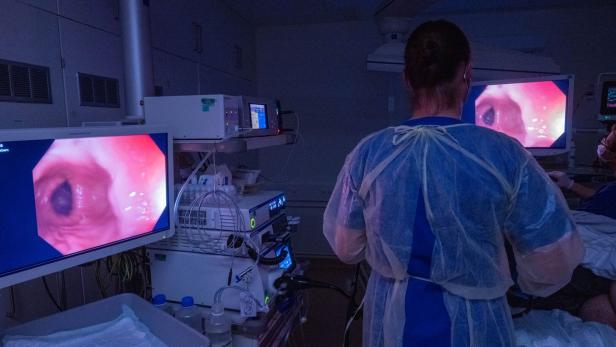 Ärztin in OP-Kleidung beobachtet Endoskopie auf zwei Monitoren im dunklen OP-Saal.