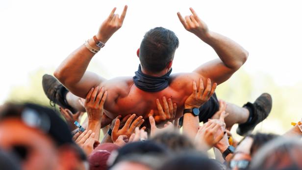 Viele Hände tragen einen Mann beim Crowdsurfing, während er die Hände zum Rockgruß hebt.