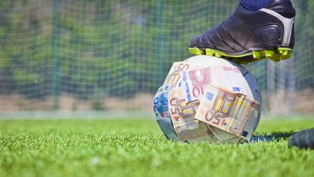 Ein Fußball wird von einem Fuß gestoppt und ist mit Geldscheinen beklebt.