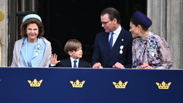 Königin Silvia, Prinz Oscar, Prinz Daniel und Kronprinzessin Victoria stehen auf einem Balkon mit königlichem Wappen und winken der Menge zu.