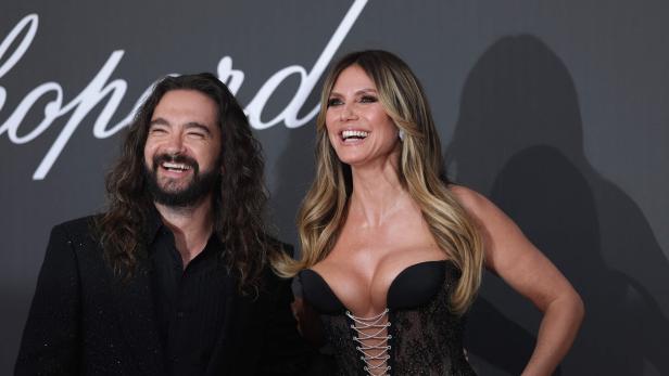Heidi Klum und Tom Kaulitz lachen gemeinsam vor einem Chopard-Hintergrund in die Kamera.