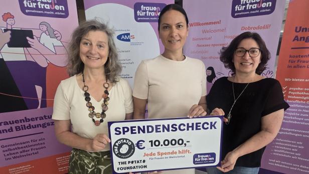 Drei Frauen halten einen Spendenscheck über 10.000 Euro vor Infotafeln von Frauen für Frauen.