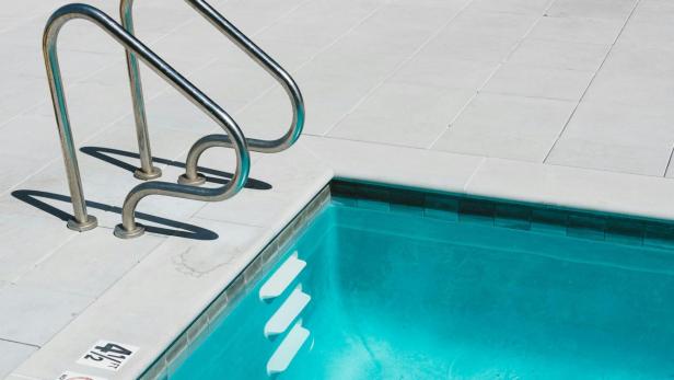 Leerer Swimmingpool mit Metallleiter und Stufen am Beckenrand bei Tageslicht.
