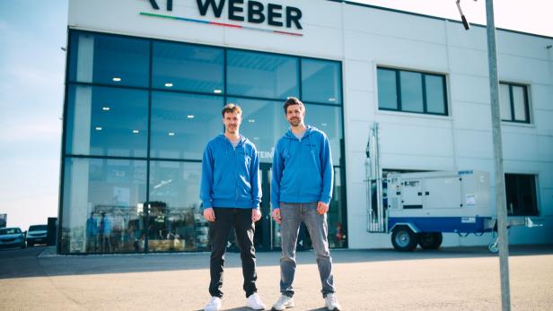 Zwei Männer in blauen Kapuzenjacken stehen vor einem modernen Firmengebäude mit der Aufschrift „RT Weber“.