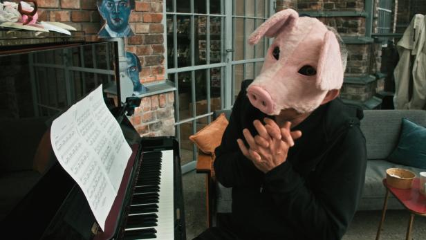 Ein Mann mit Schweinchenmaske sitzt am Klavier.