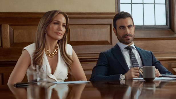 Jennifer Lopez und Brett Goldstein sitzen an einem Tisch nebeneinander, er hält einen Kaffeebecher in der Hand.
