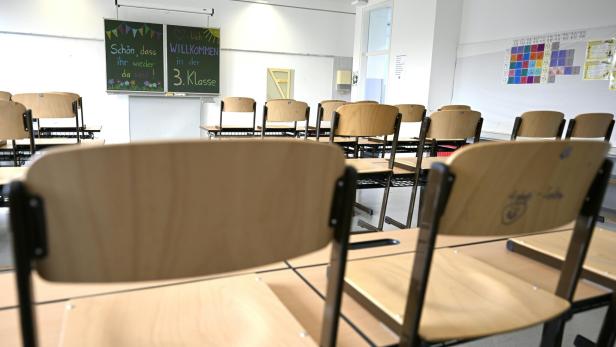 Leerer Klassenraum mit hochgestellten Stühlen und einer Tafel, auf der eine Willkommensbotschaft für die 3. Klasse steht.